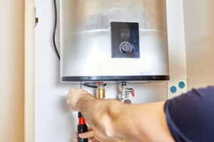 A plumber Boone County uses a screwdriver to repair or install a modern wall-mounted water heater with visible pipes and a digital control panel.